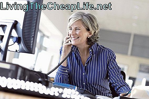Moden kvinde bruger telefon på skrivebordet i kontor, smilende